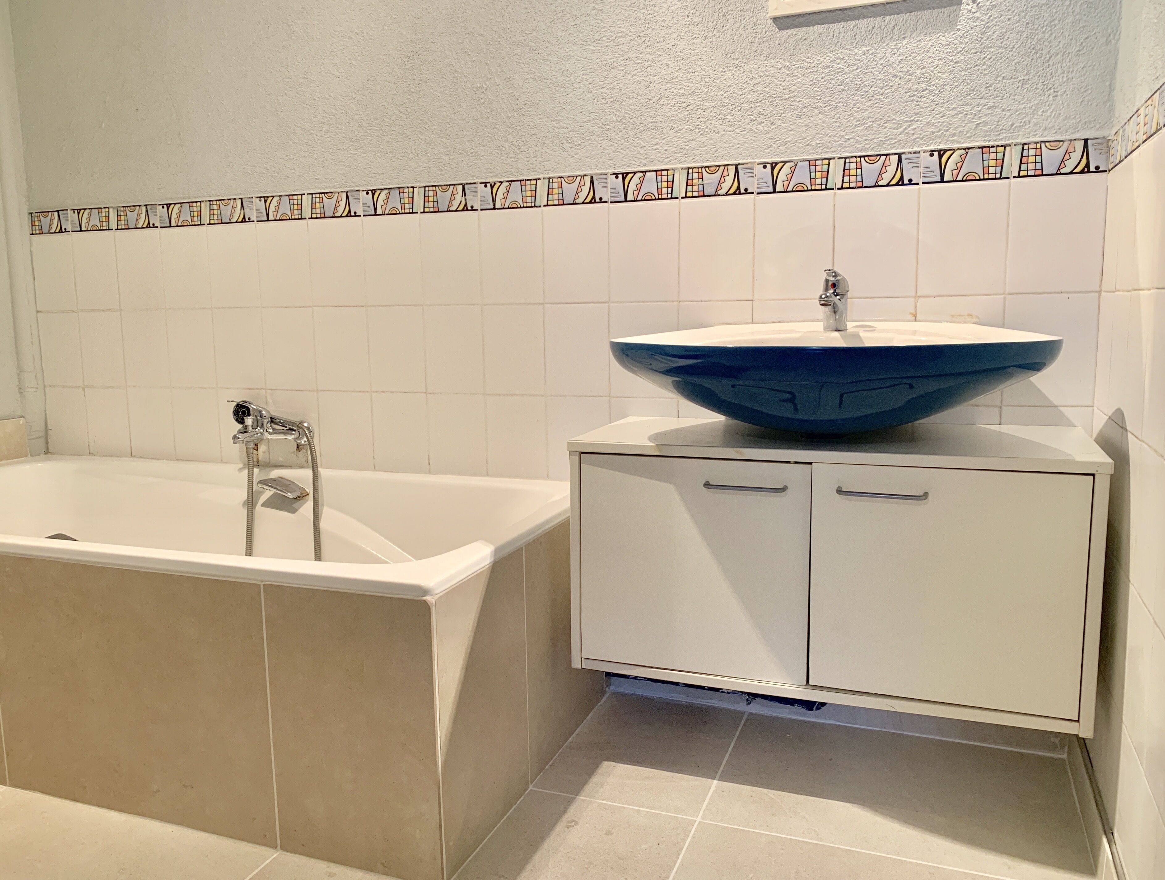 A bathroom with a bathtub, a white sink with a blue basin, and a cabinet with two drawers.