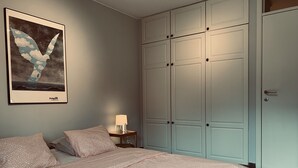 Quarto com cama, mesa de cabeceira, abajur, guarda-roupa e um quadro na parede.