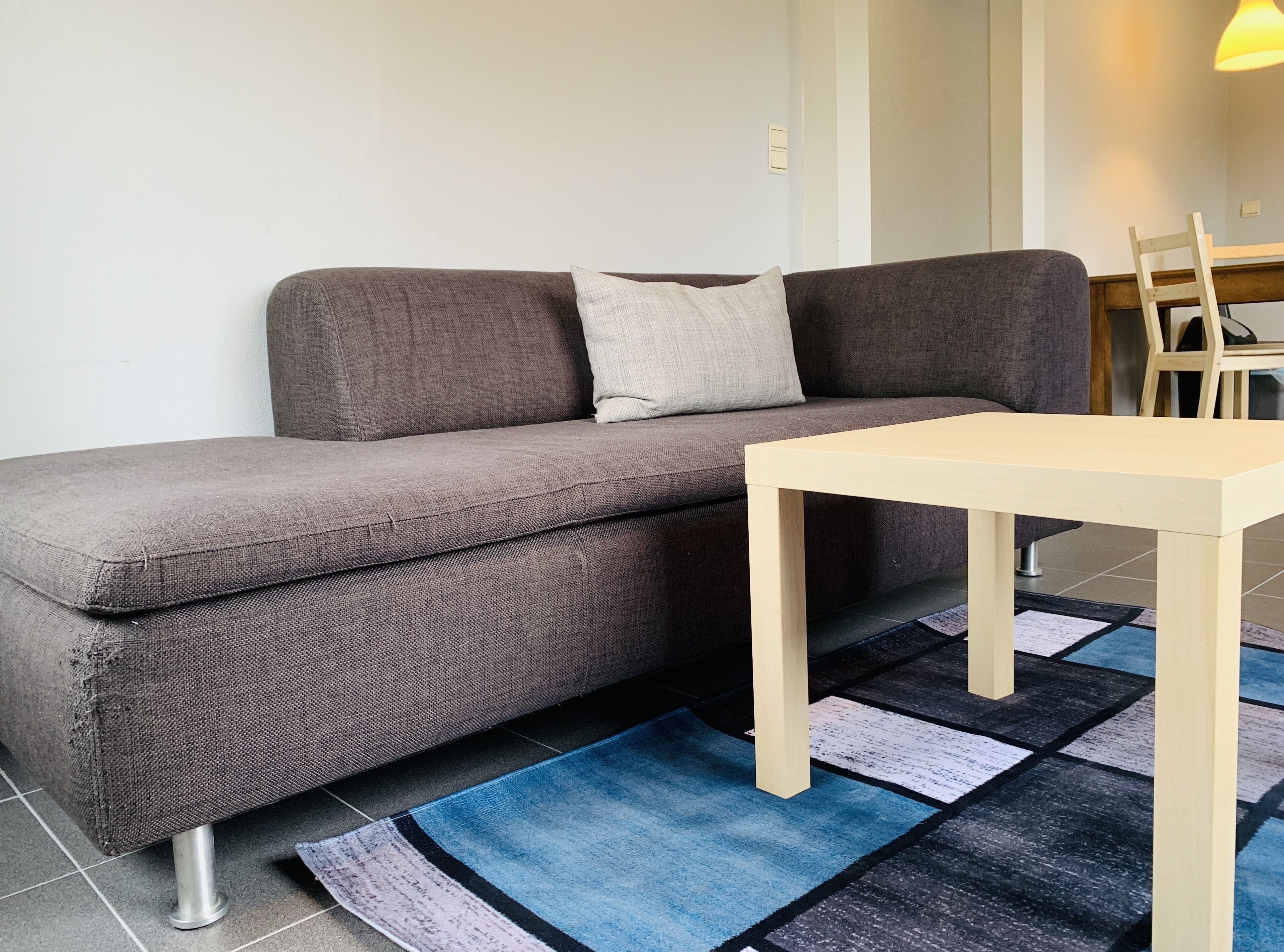A grey sofa with a light cushion, a wooden table, and a patterned rug.