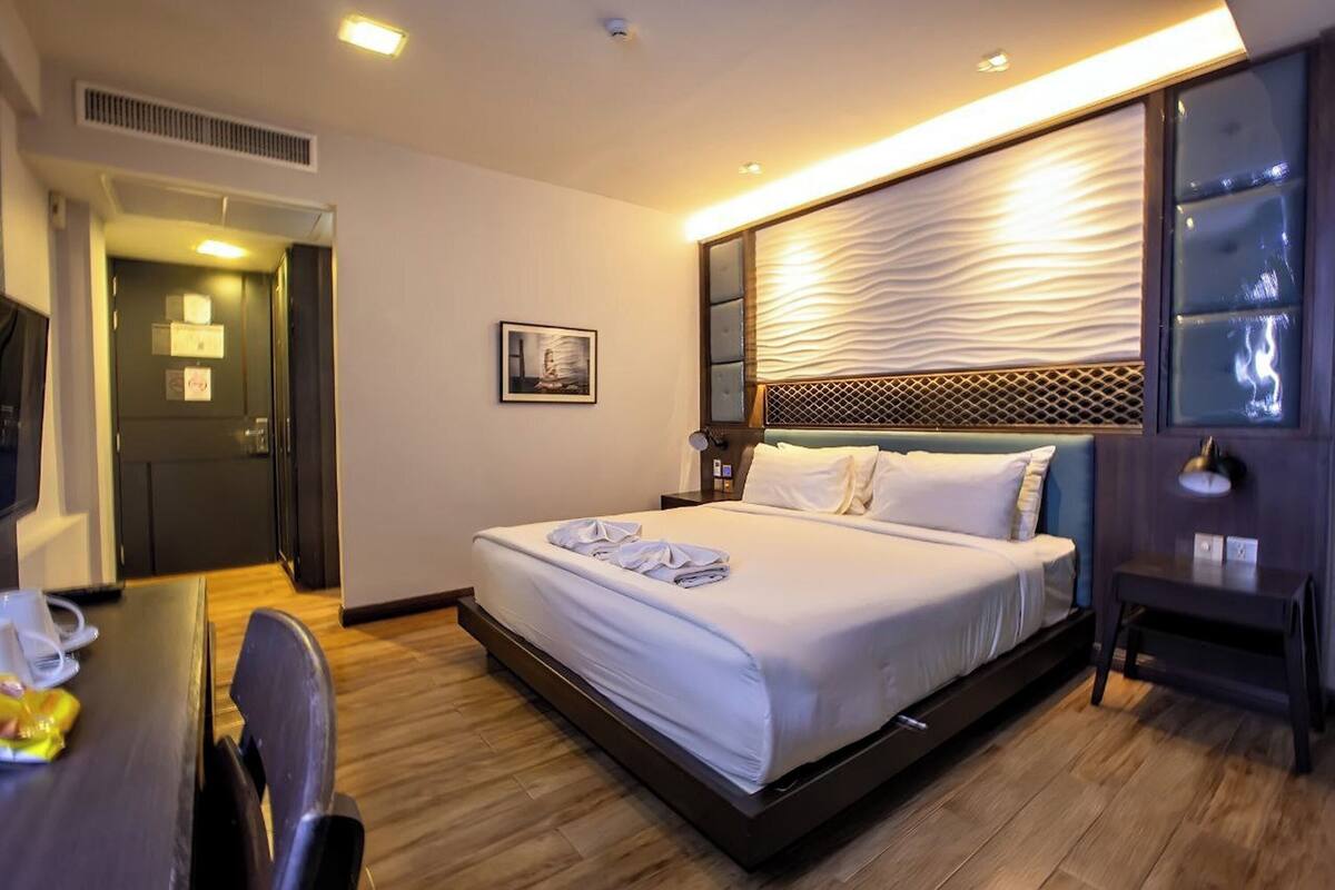 A hotel room with a bed, bedside table, chair, and a desk with a chair.