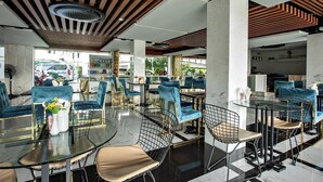 Un restaurante moderno con mesas redondas y sillas de terciopelo azul, que cuenta con un techo de madera y vistas a la calle.