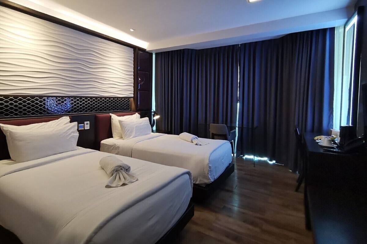 A hotel room with two beds, a desk, a chair, and a large window with curtains.