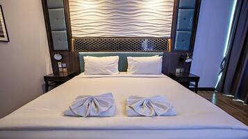 A hotel room with a large bed, two pillows, a headboard with a textured design, and a nightstand with a lamp.