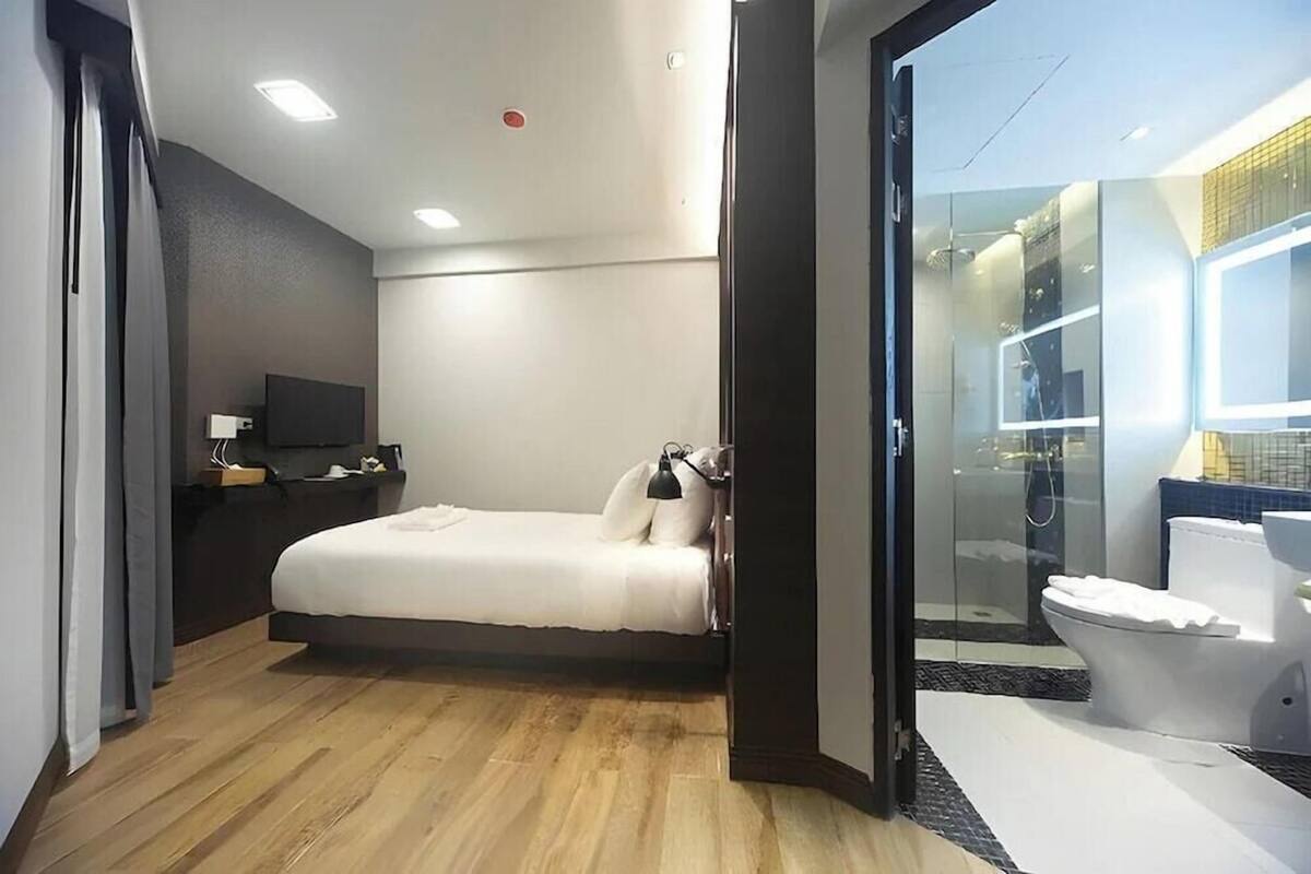 A modern hotel room with a bed, bedside table, TV, and a glass-enclosed shower area.