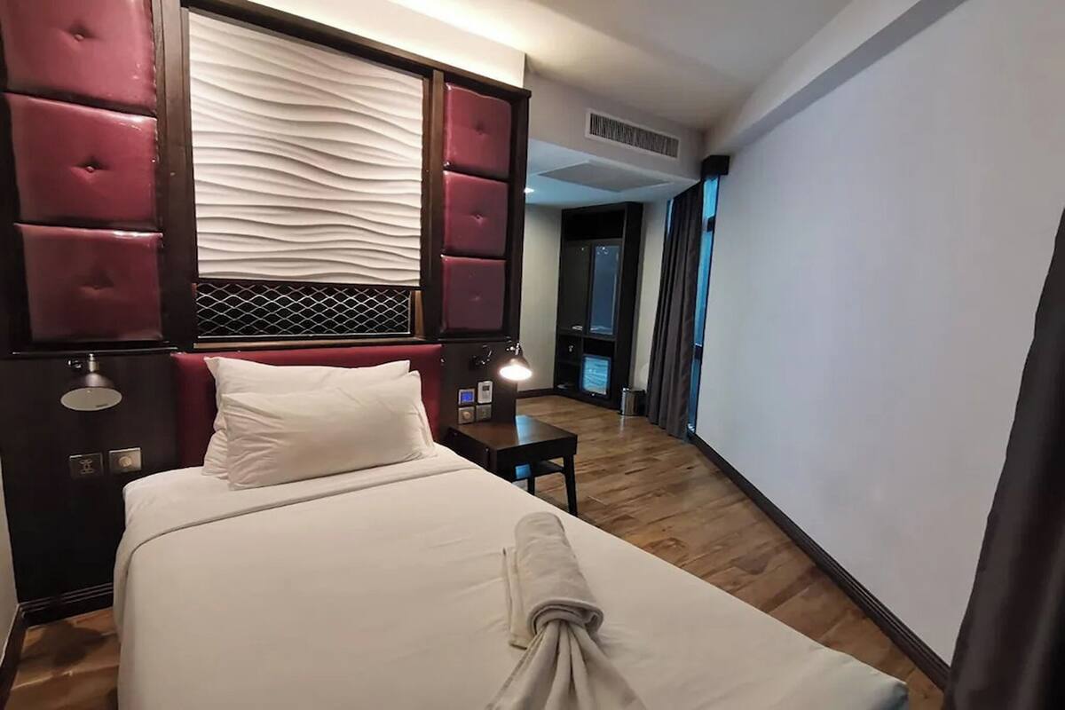 A hotel room with a bed, a bedside table, a lamp, and a television.