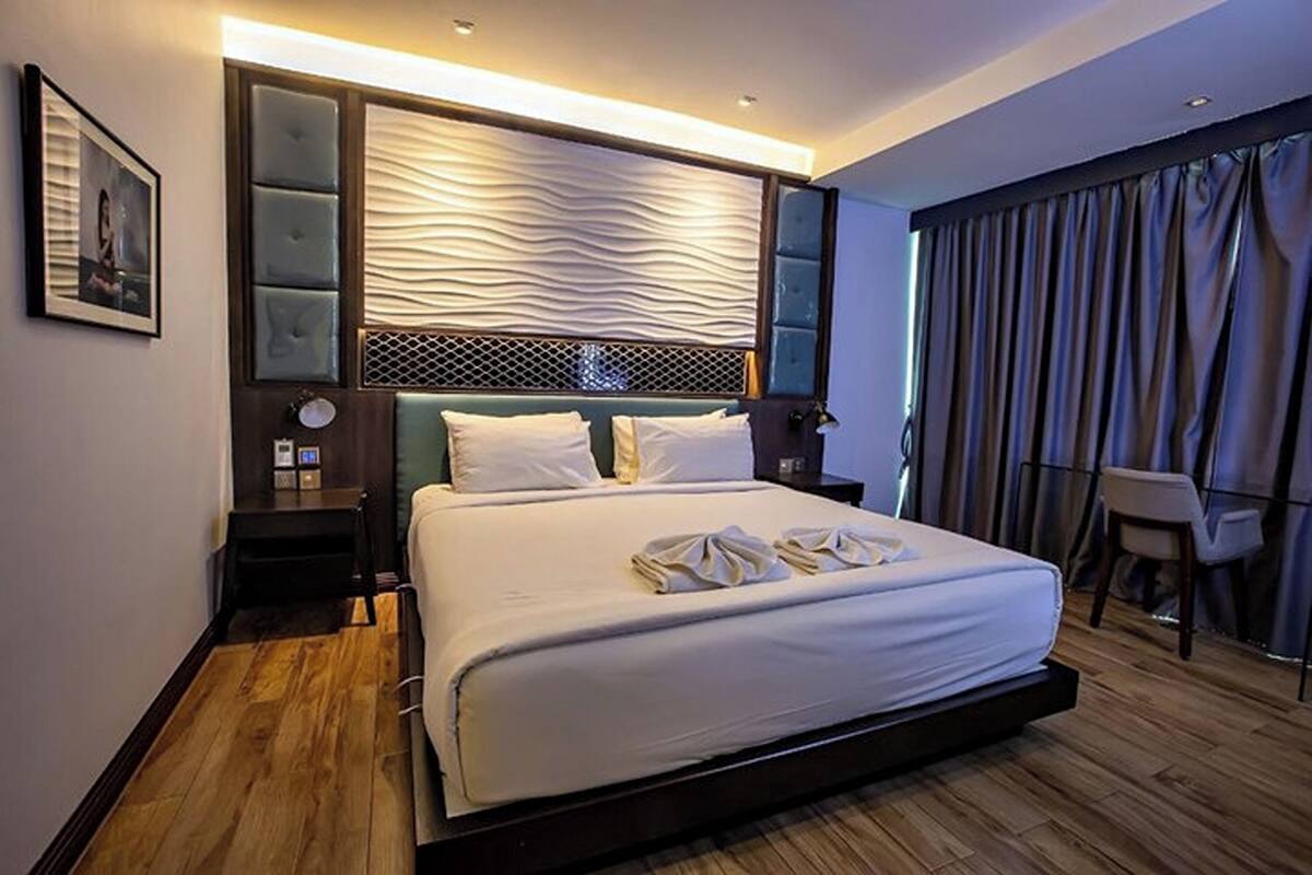A modern hotel room with a large bed, a nightstand, a desk, and a chair.