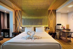 Una habitación de hotel con una cama grande, un escritorio y una silla. Hay un panel decorativo sobre la cama y una pequeña mesa con una lámpara.
