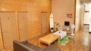 Una habitación con paredes de madera, un sofá, una mesa, una tabla de surf, un televisor y un ventilador.