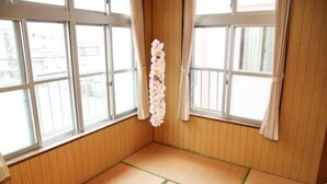 Una habitación con suelo de esteras de tatami, paredes de madera y ventanas amplias con cortinas.