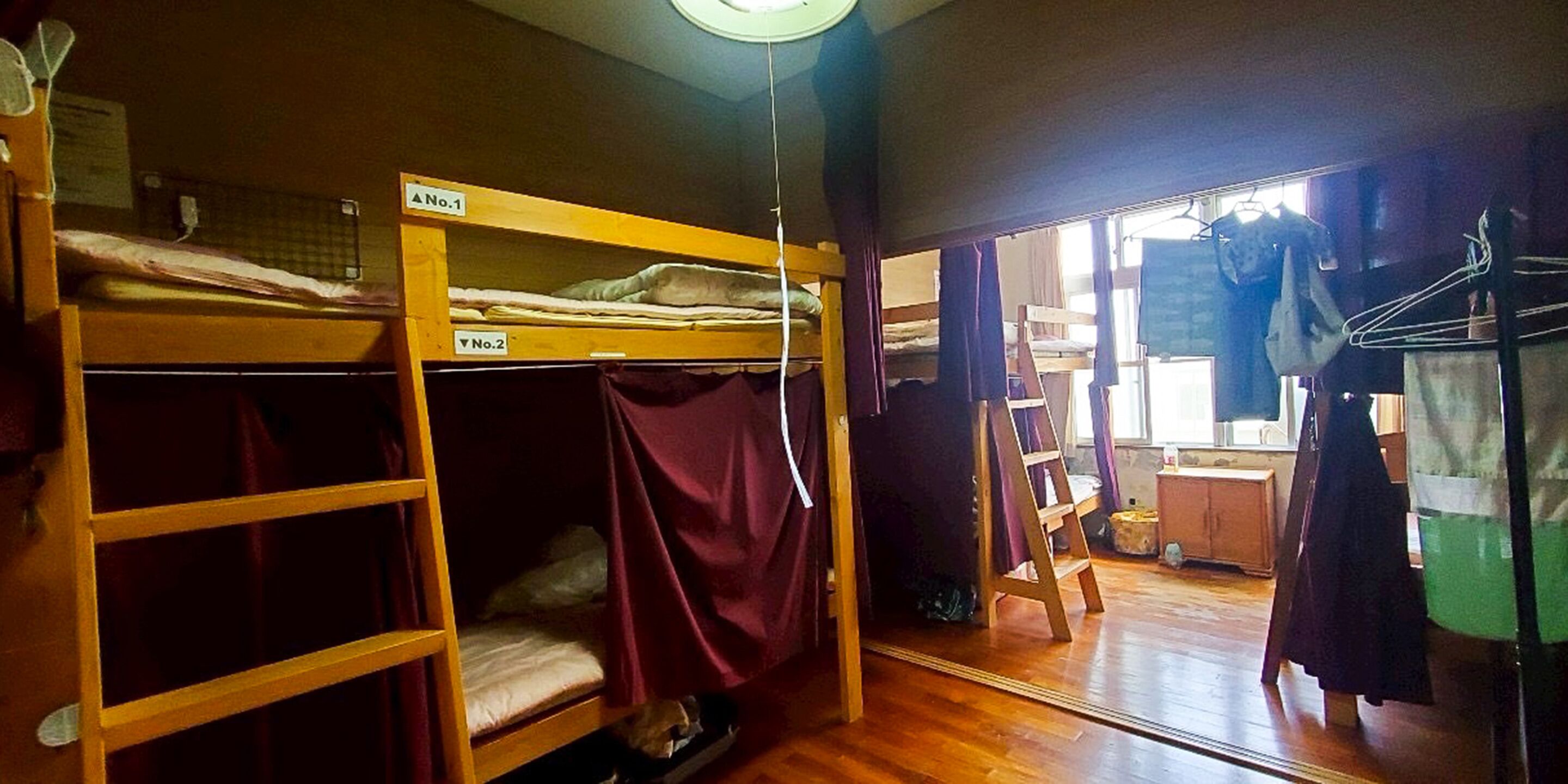 A dormitory room with bunk beds, a wooden floor, and a mirror reflecting the room.