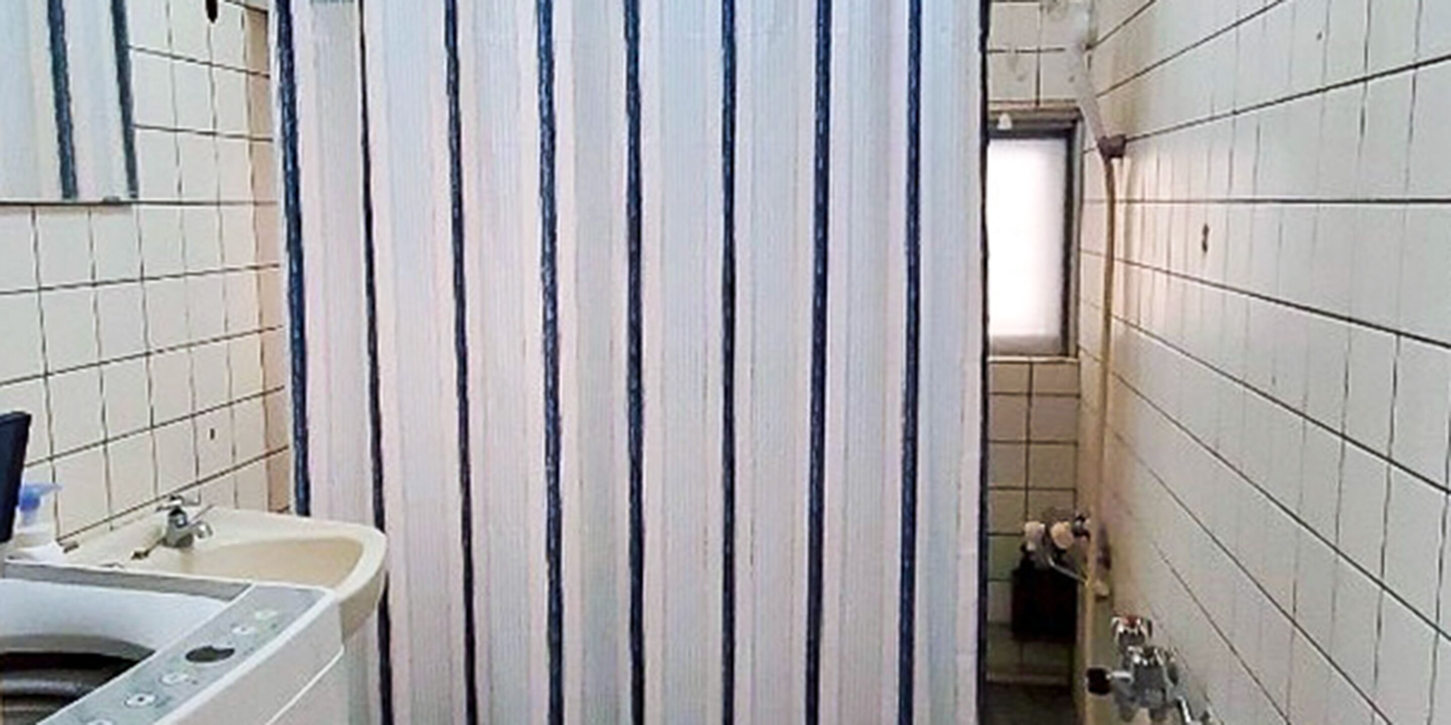 A narrow bathroom with a sink, mirror, and a shower stall.