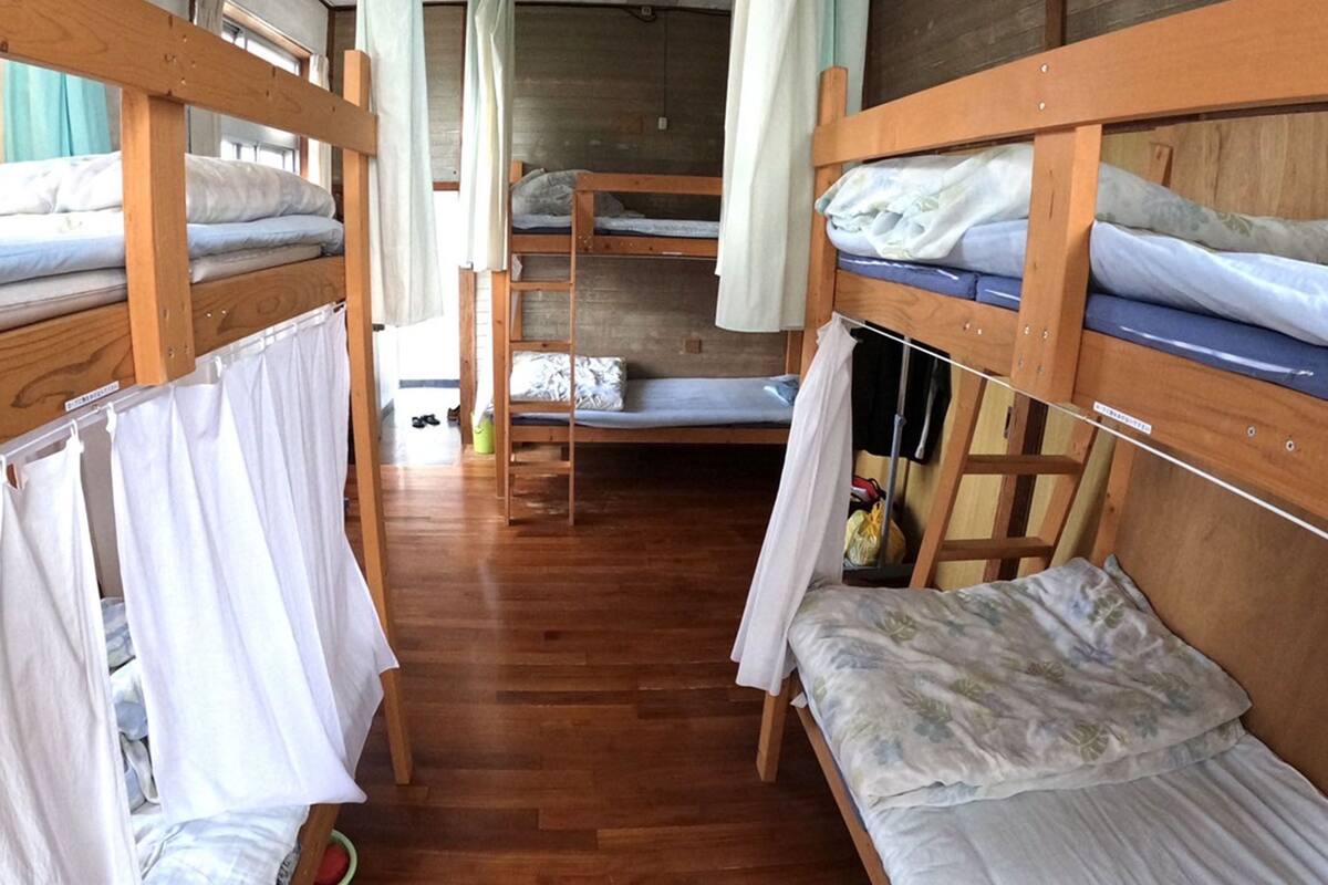 A narrow corridor with bunk beds on either side, wooden flooring, and curtains on the beds.