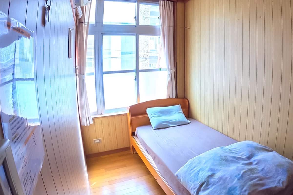 A small, single-bed room with wooden walls and a window.