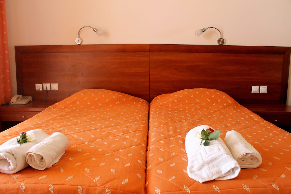 A double bed with an orange bedspread and two neatly folded white towels with a flower on each.
