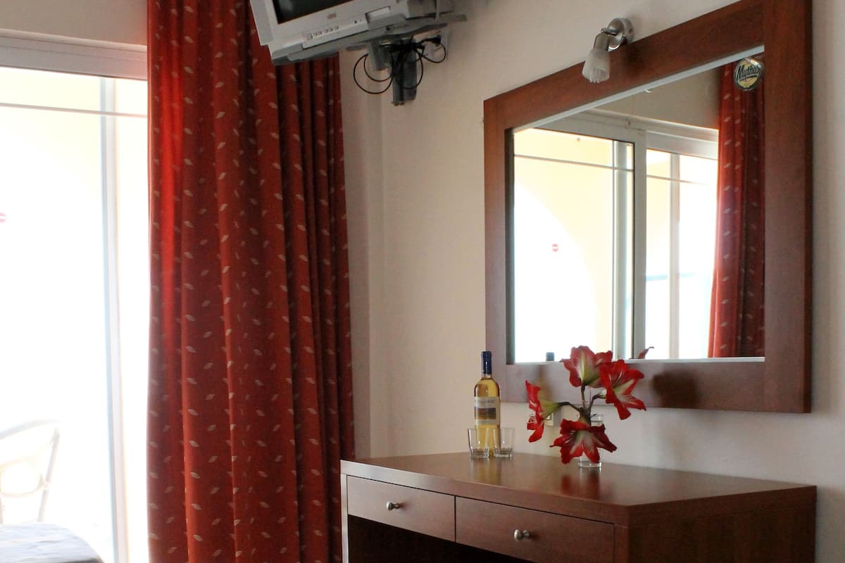 A hotel room with two beds, a TV mounted on the wall, a wooden desk, a mirror, and a window with red curtains.