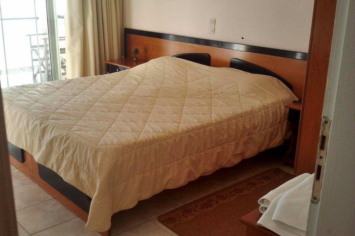 A hotel room with a bed, a nightstand, a small table, and a window with curtains.
