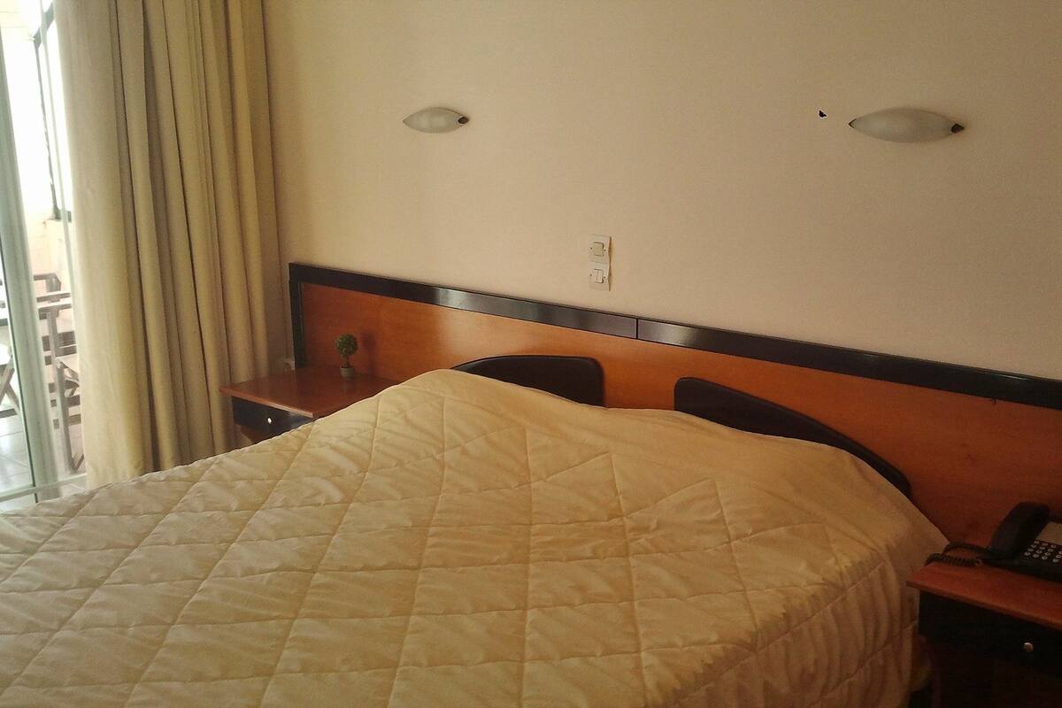 A hotel room with a bed, a bedside table with a lamp, and a phone.