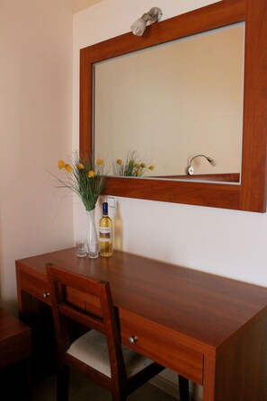 Ein Holztisch mit einem Spiegel darüber, eine Vase mit Blumen und eine Flasche Alkohol.