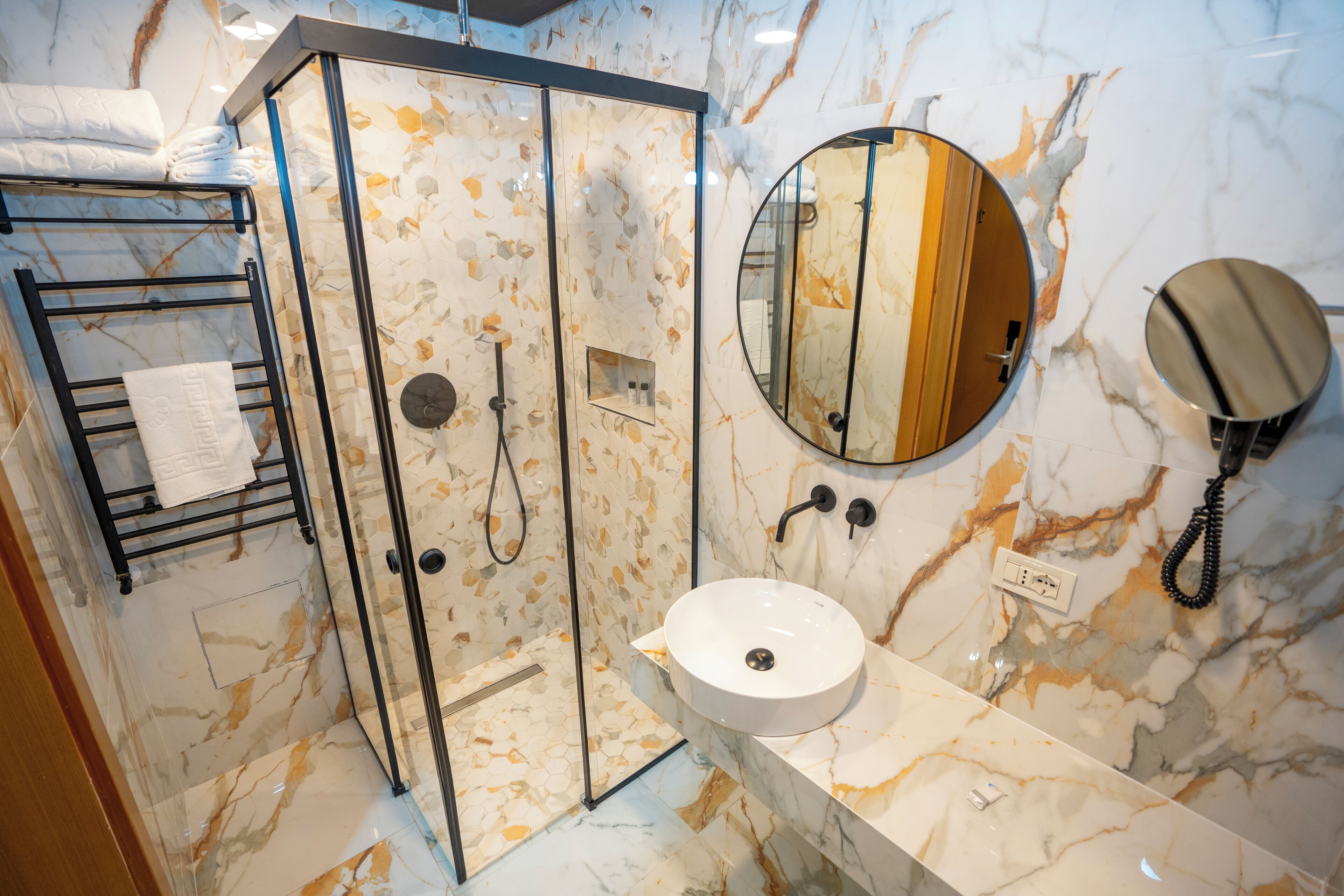 Un baño con ducha de vidrio, un lavamanos con encimera de mármol y un espejo redondo.