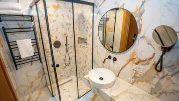 Un baño con ducha de vidrio, un lavamanos con encimera de mármol y un espejo redondo.