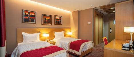 A hotel room with two beds, a desk, and a chair. There are three framed pictures on the wall.