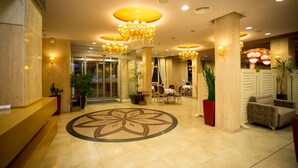 Un hall d’hôtel doté d’un grand motif floral en mosaïque, de plusieurs lustres et d’espaces aménagés avec des sièges.