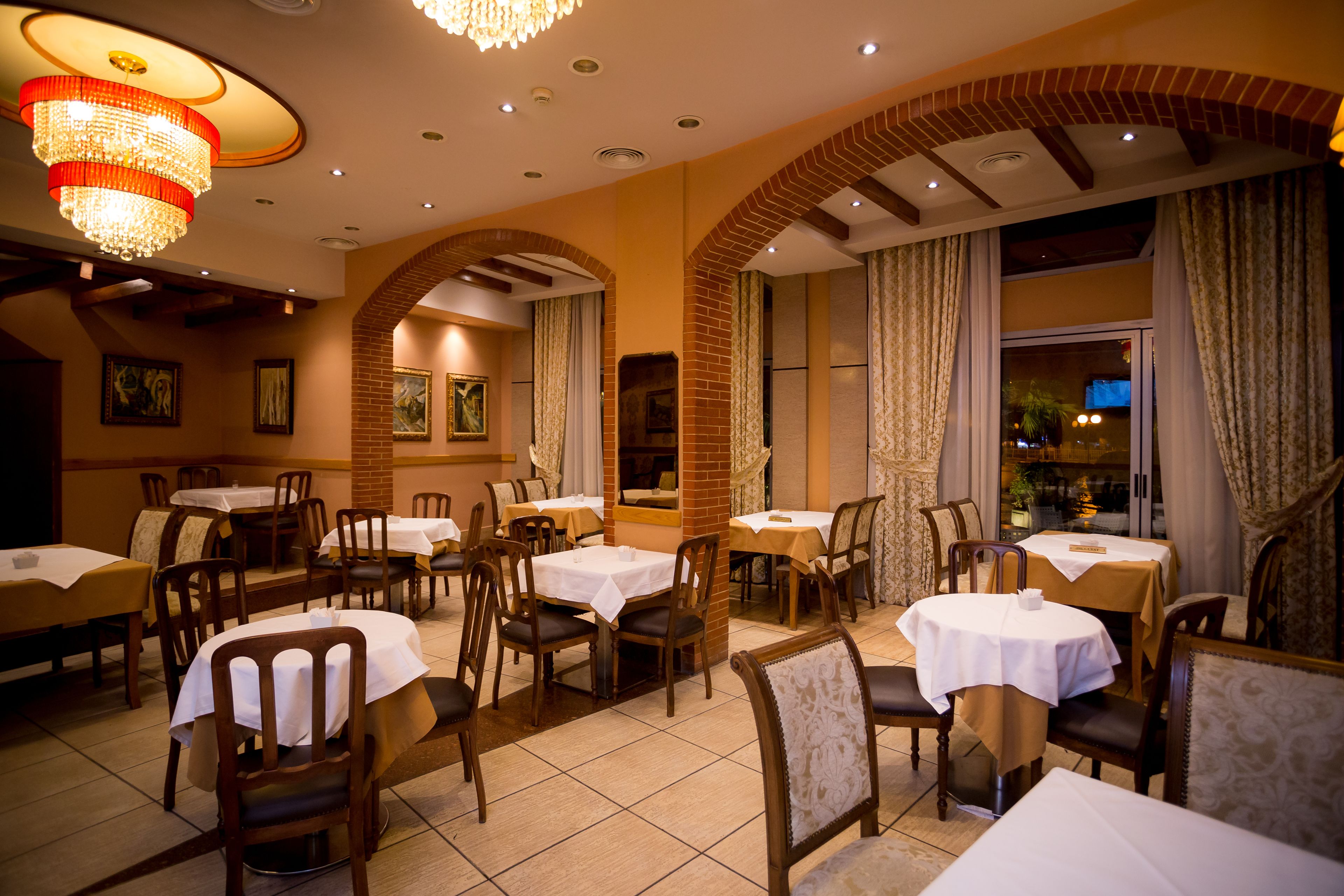 A restaurant with multiple tables and chairs, brick arches, and a chandelier.