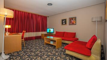 Une chambre d’hôtel avec un rideau rouge, une télévision, un bureau, un canapé et une moquette à motifs.