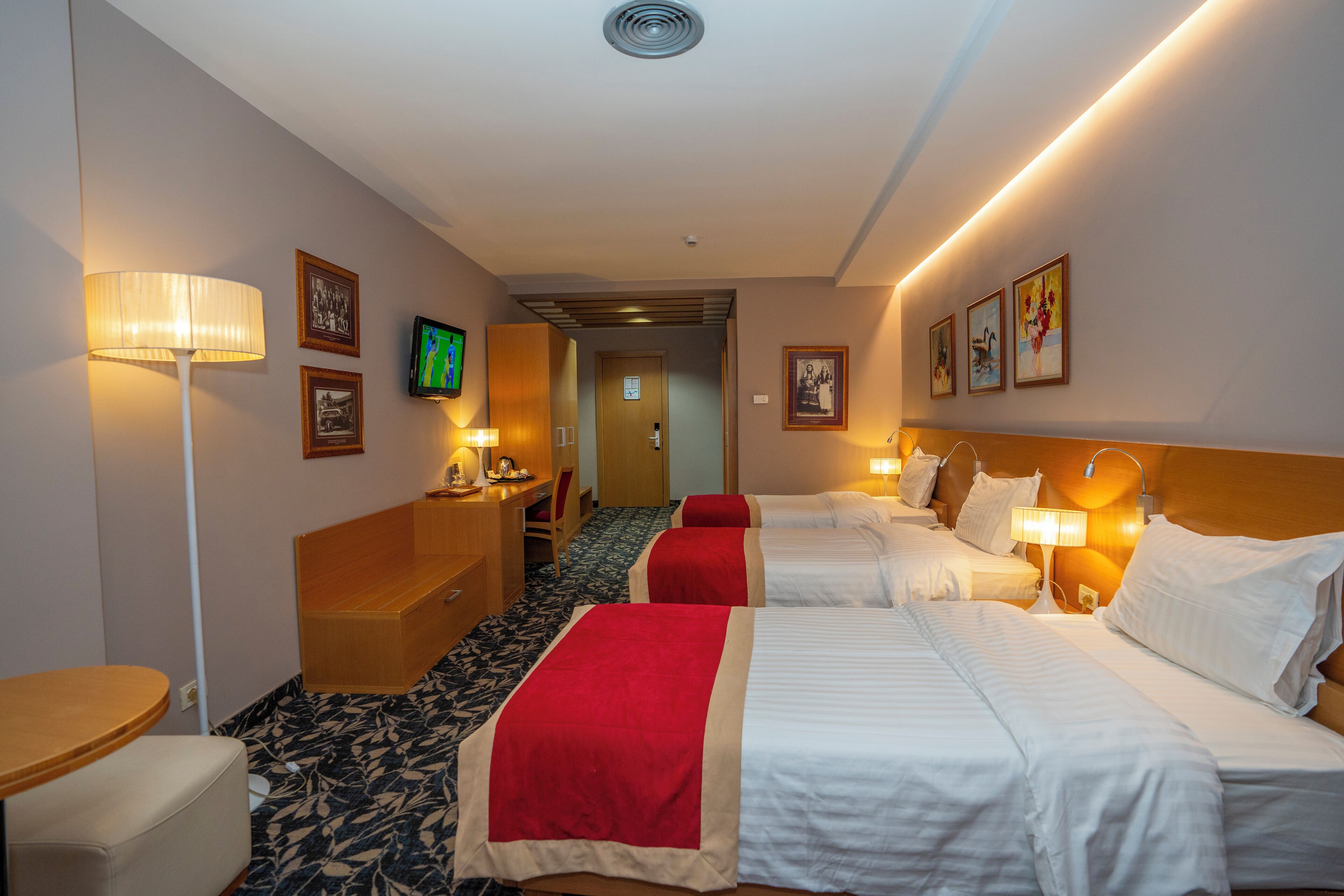 A hotel room with two beds, a desk, a chair, and a television.