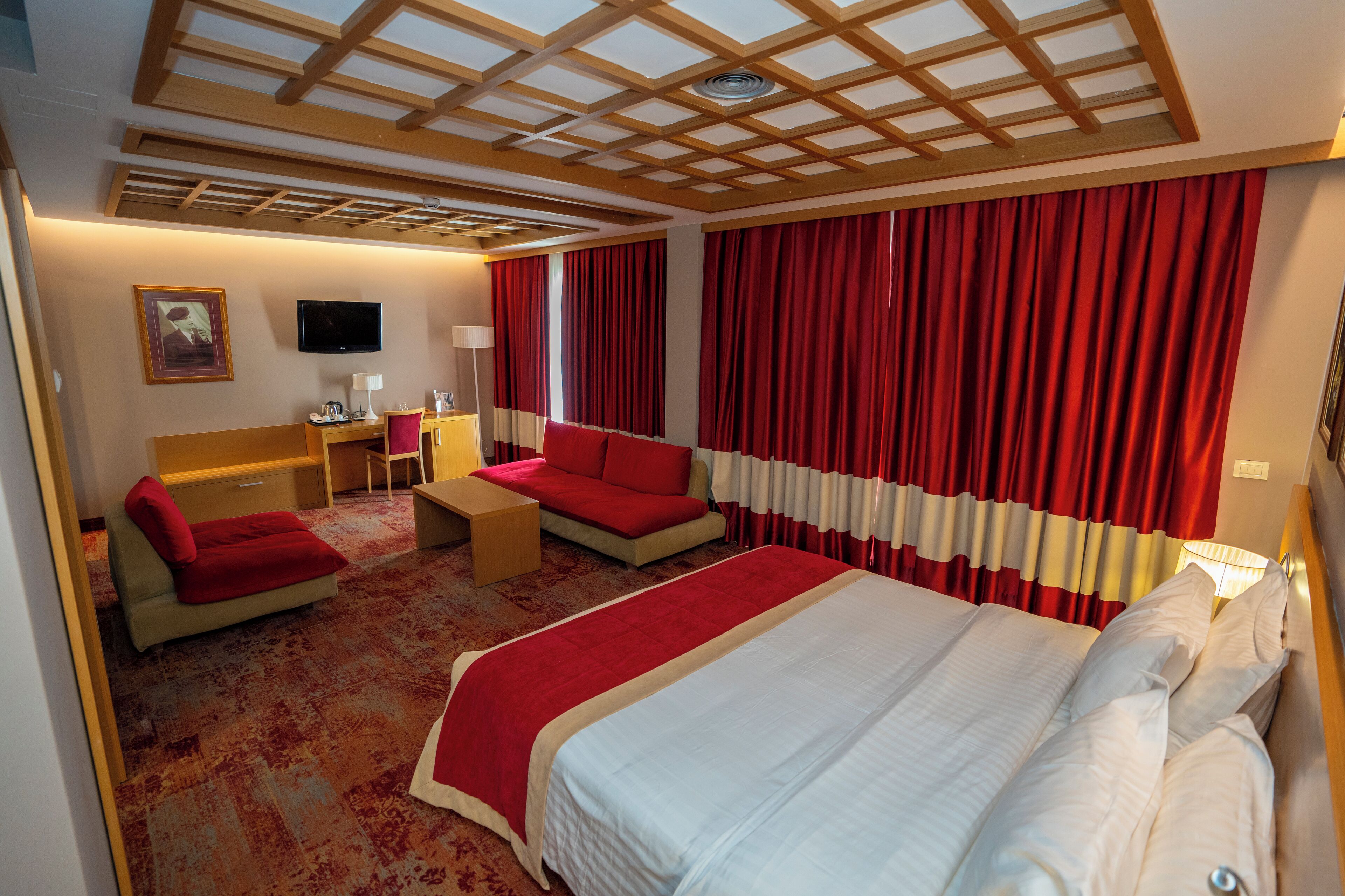 A hotel room with a large bed, a sofa, a desk, and a TV.