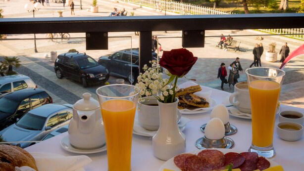 Une table de petit-déjeuner avec divers aliments et boissons, donnant sur une rue animée et des immeubles.