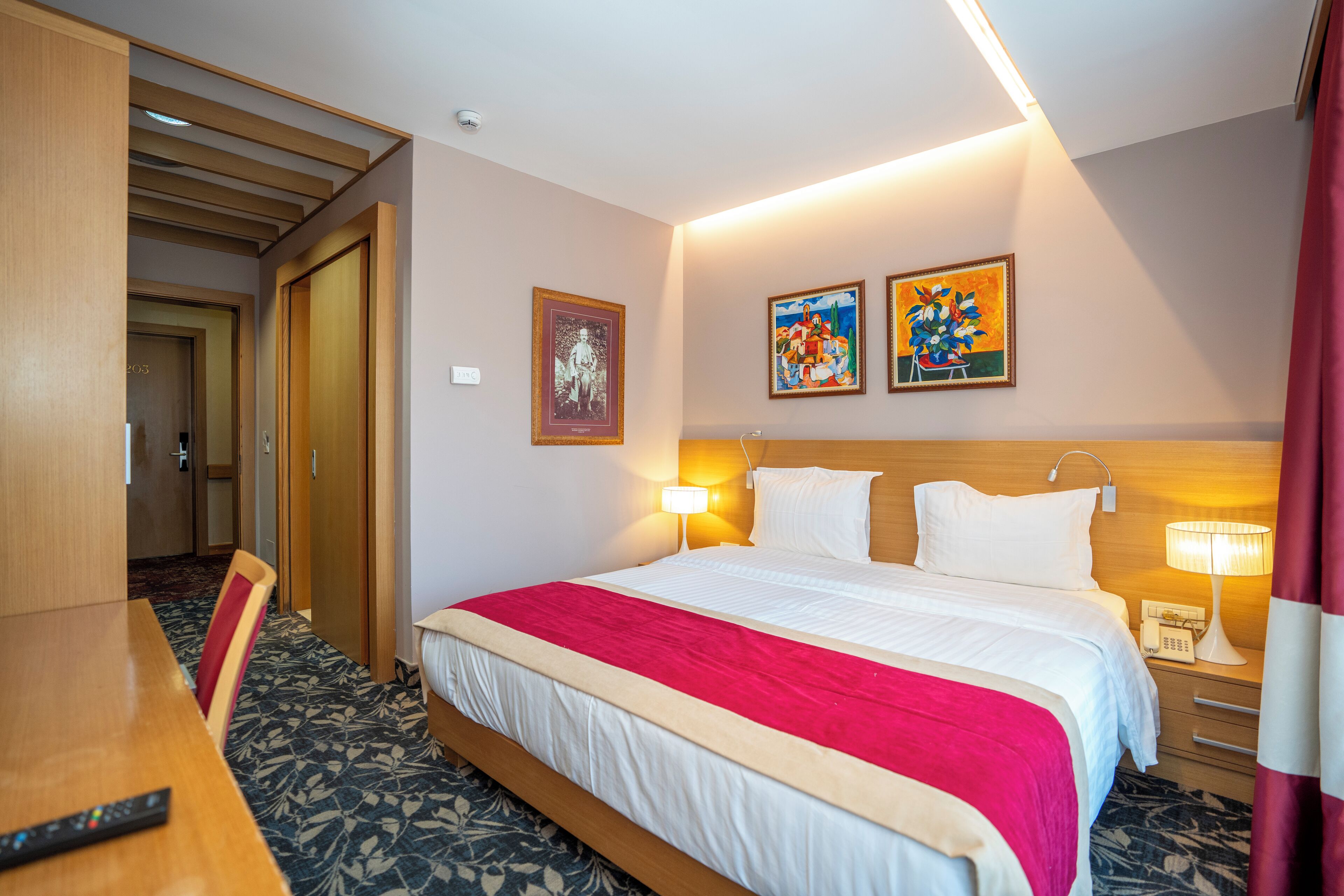 Ein Hotelzimmer mit einem großen Bett, Nachttischen, einem Schreibtisch und einem Sessel.