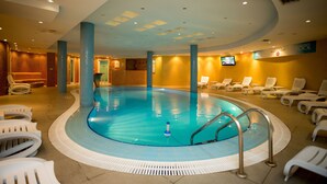 Une piscine intérieure avec un sol carrelé, des chaises longues et un écran de télévision fixé au mur.