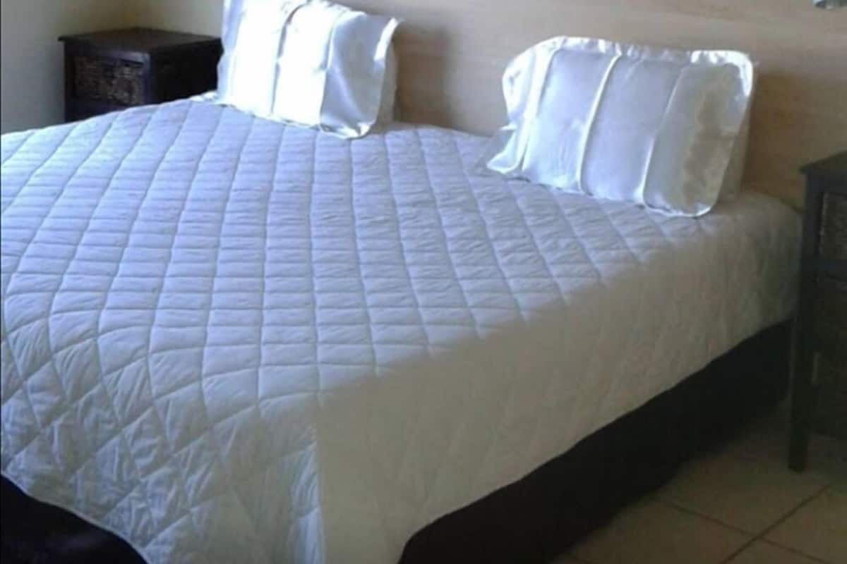 A neatly made bed with a quilted white bedspread and two pillows.
