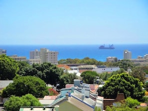 A coastal cityscape with buildings, trees, and a large ship in the distance.