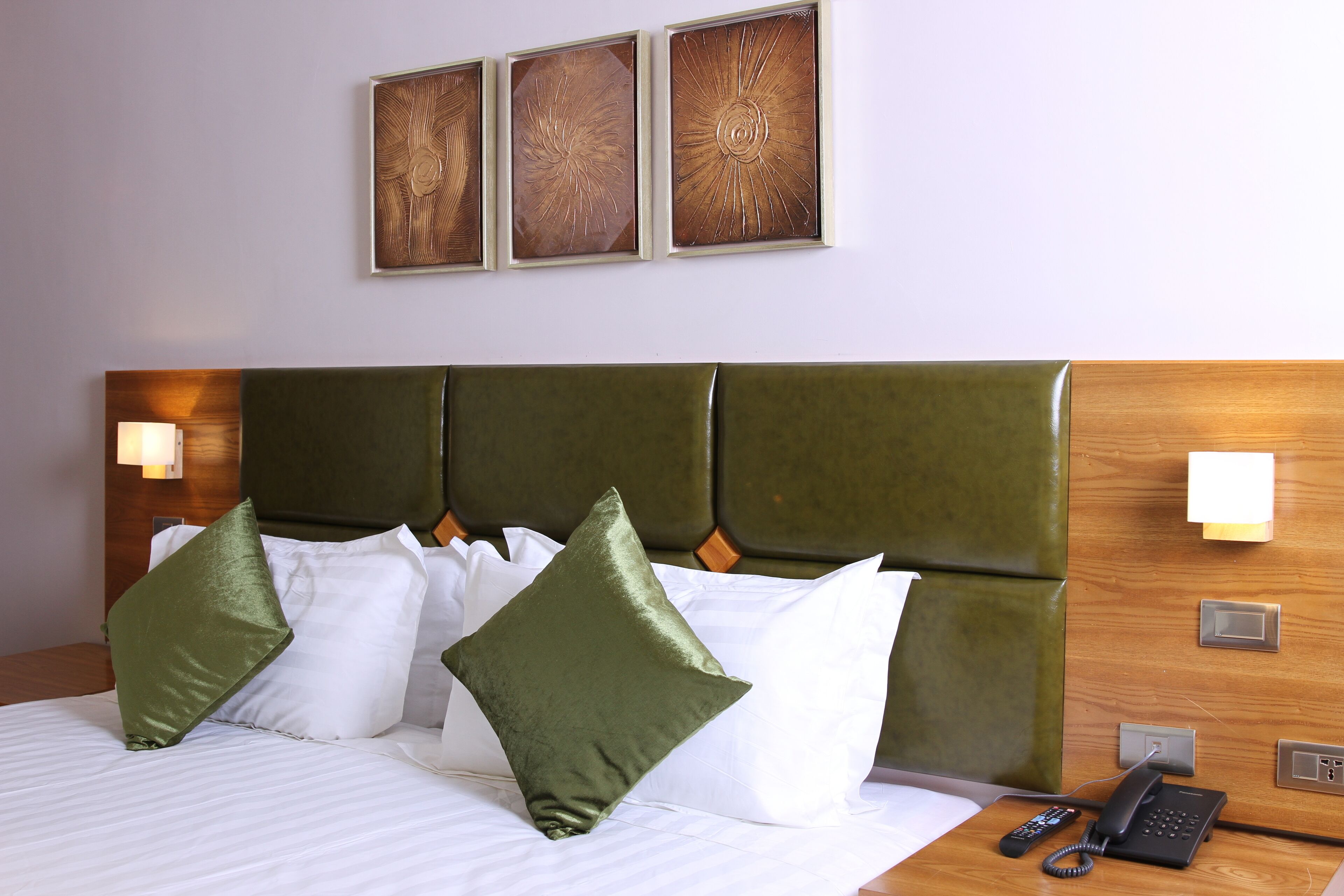 Une chambre d’hôtel avec une tête de lit recouverte d’un tissu vert, du linge de lit blanc et un téléphone sur la table de chevet.