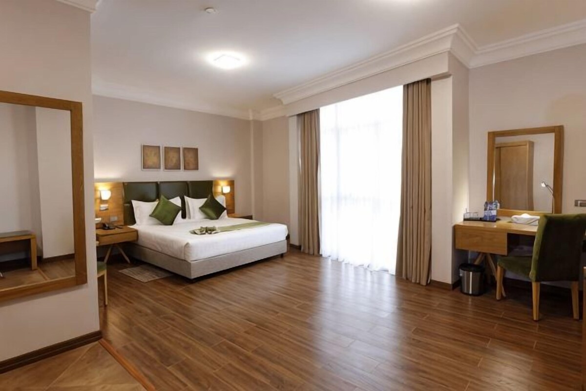 A hotel room with a bed, bedside table, lamp, desk, chair, and a large mirror.