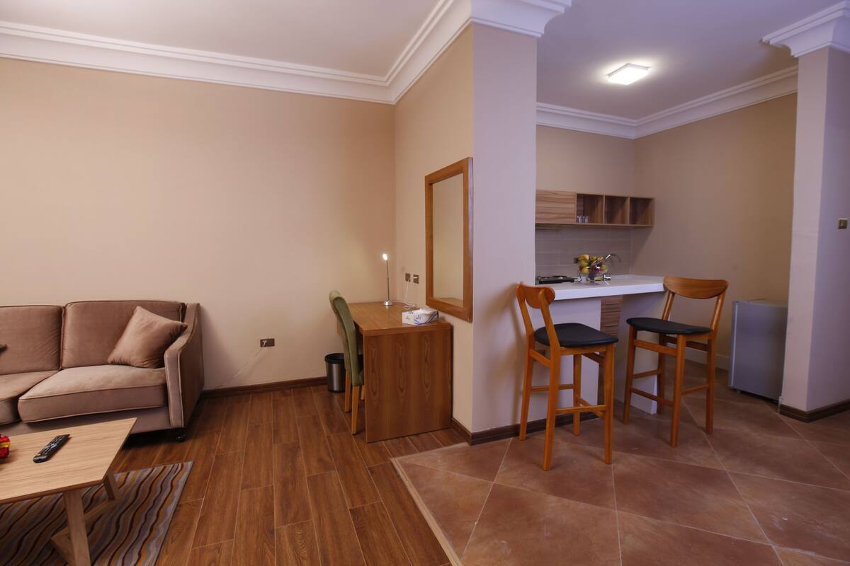 A living room with a sofa, a dining table, and two chairs. There is a kitchen area with a counter and cabinets.