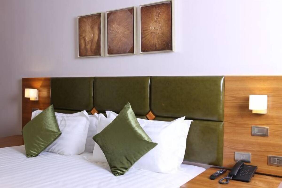A hotel room with a bed, green headboard, white bedding, and a phone on the nightstand.
