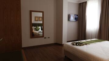 Une chambre d’hôtel avec un grand lit, une armoire en bois, un miroir, une télévision et une fenêtre avec des rideaux.