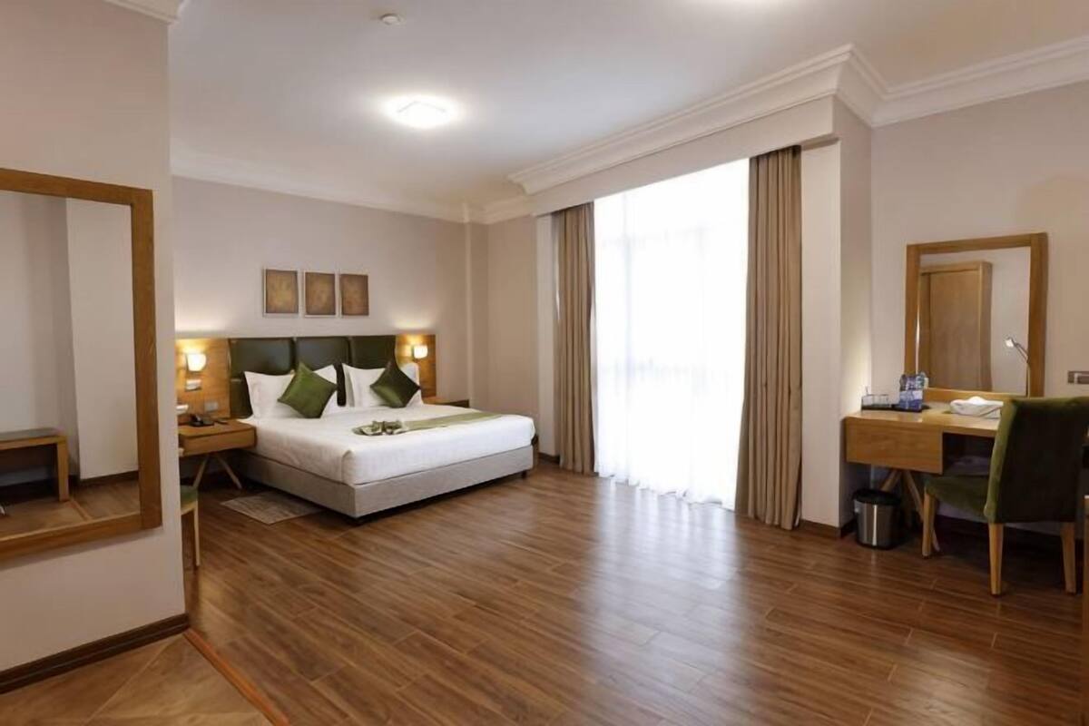 A hotel room with a bed, bedside table, lamp, desk, chair, and a large mirror.