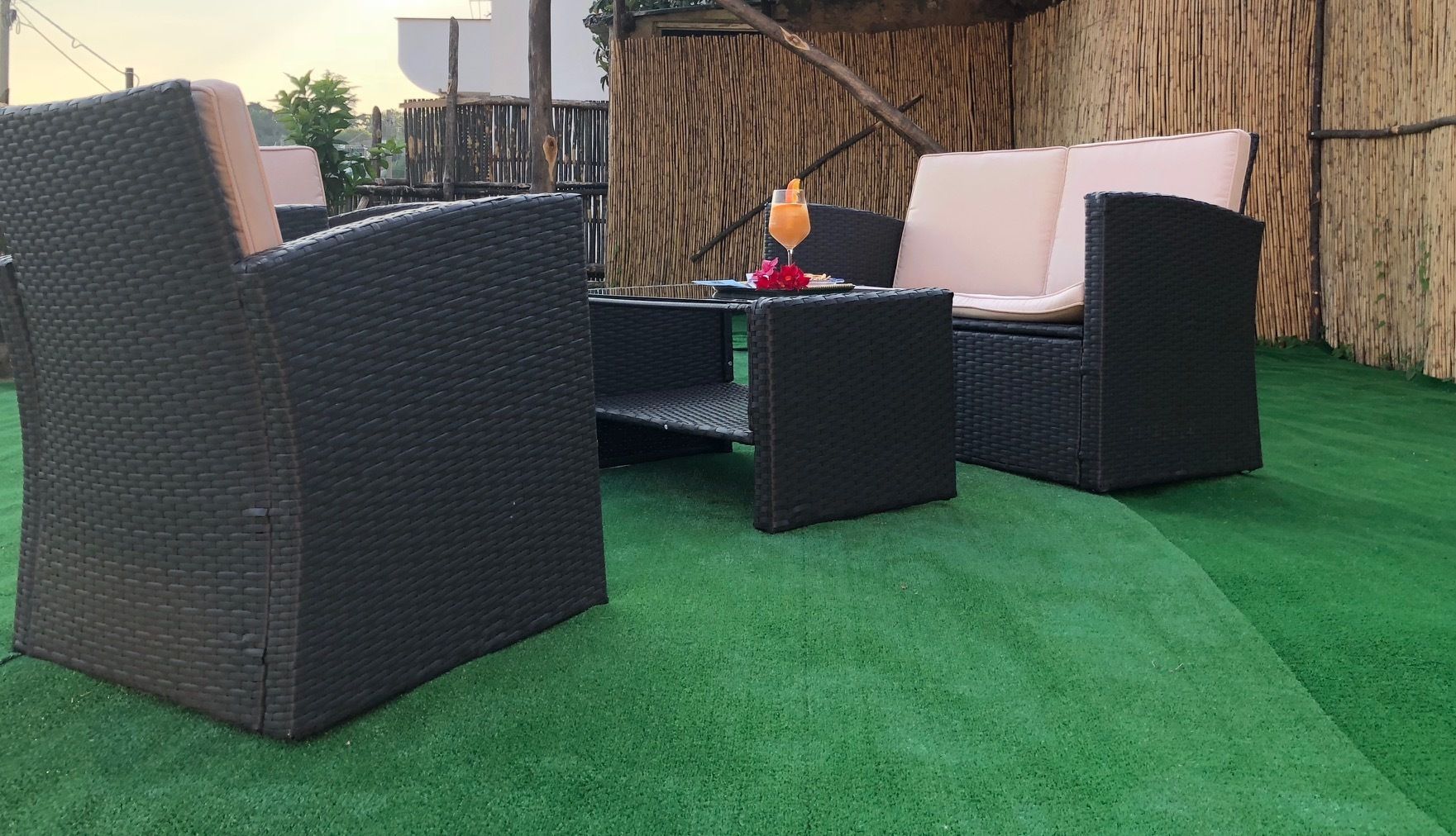 Un área de patio con mobiliario de mimbre y una mesa, rodeada por una valla de bambú.