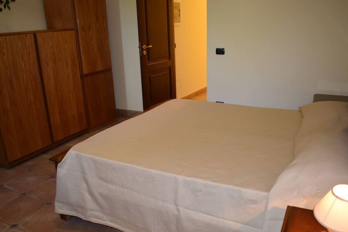 A bedroom with a bed, wooden wardrobe, and a nightstand with a lamp.