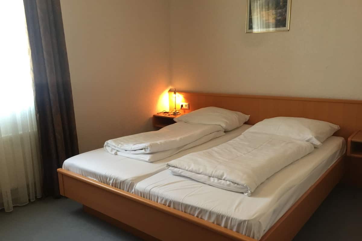 A double bed with white linens in a hotel room.