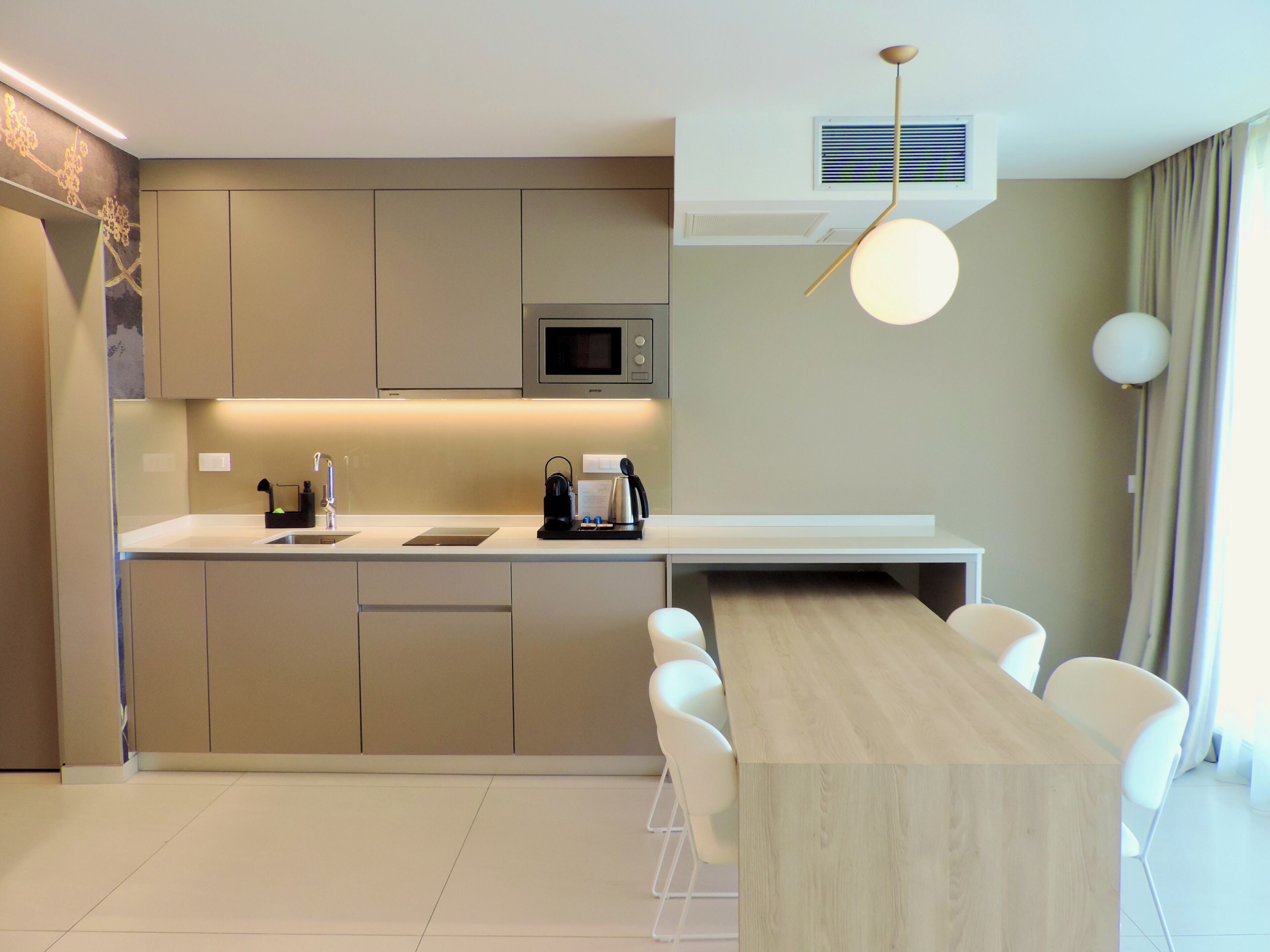 Een moderne keuken met een ingebouwde magnetron, een koffieapparaat en een eethoek met een houten tafel en witte stoelen.