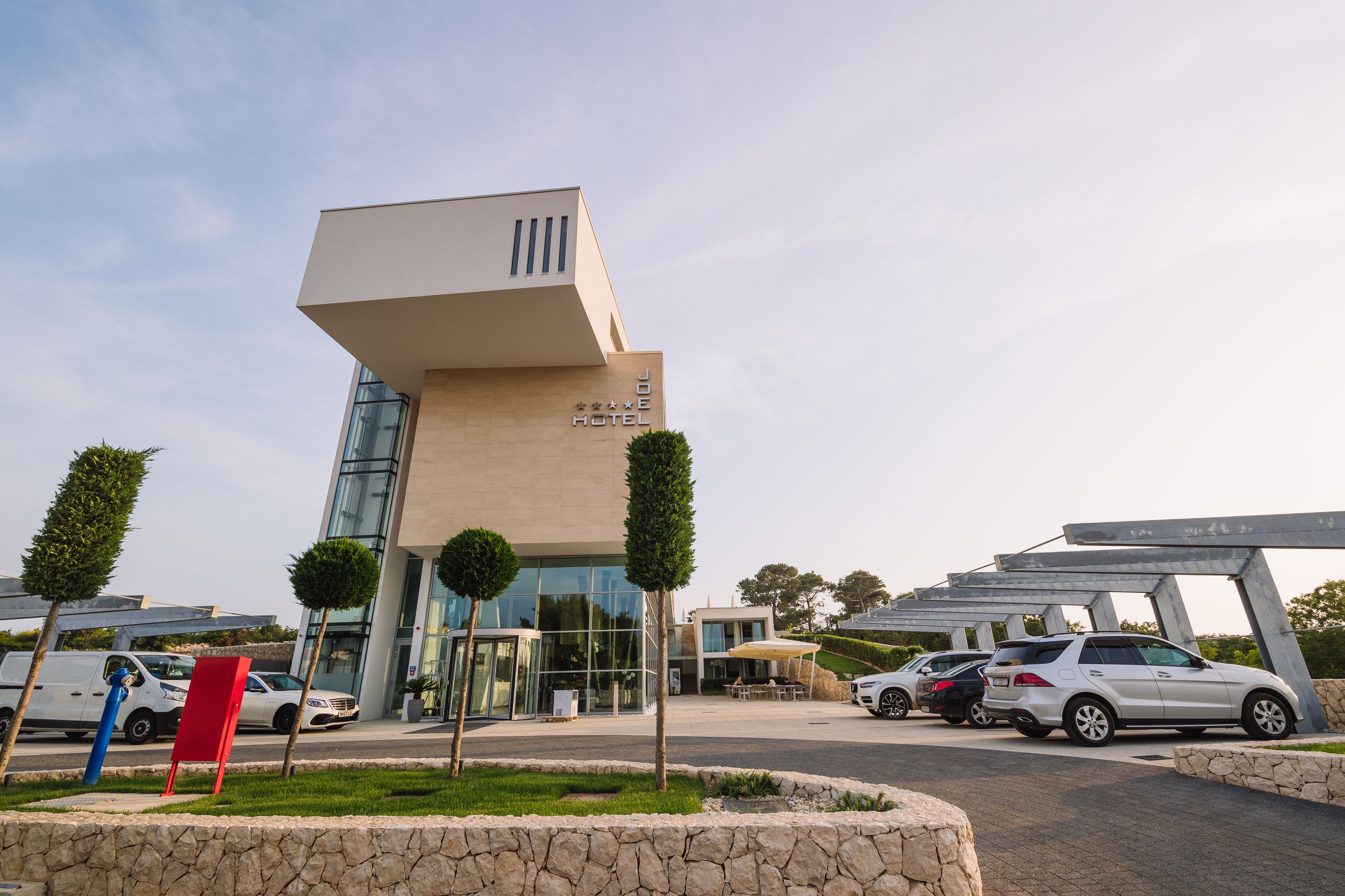 A modern hotel with a unique architectural design, featuring a prominent entrance and a parking area with several cars.