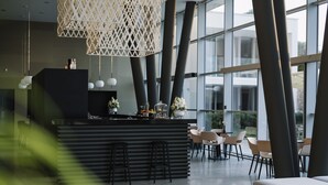 Un área de bar moderna con mostrador negro, lámparas colgantes blancas y vistas al exterior a través de amplios ventanales.
