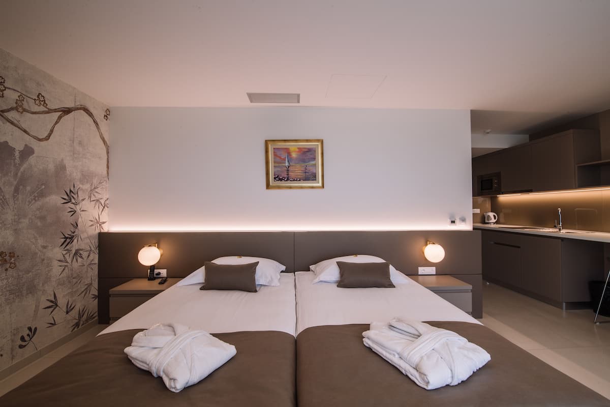 Una habitación de hotel moderna con dos camas, una kitchenette pequeña y un cuadro en la pared.