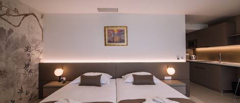 A modern hotel room with two beds, a small kitchenette, and a painting on the wall.