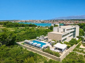 Ein modernes Hotel mit Schwimmbad, umgeben von Grün und mit Blick auf eine Küstenstadt.